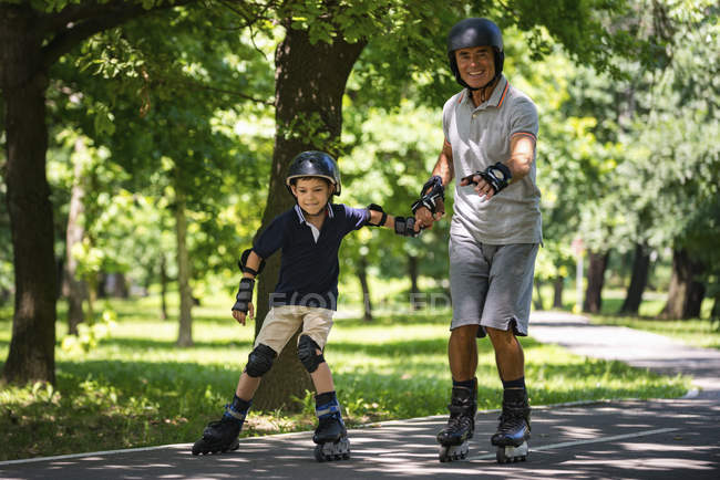 Grandfather and grandson enjoying rollerskating in summer park. — Stock Photo