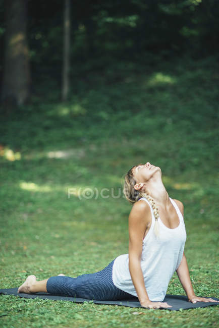 Woman doing yoga, practicing bhujangasana cobra position on mat in park. — Stock Photo
