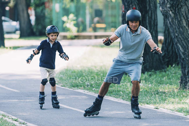 Дедушка учит внука кататься на роликах в летнем парке . — стоковое фото
