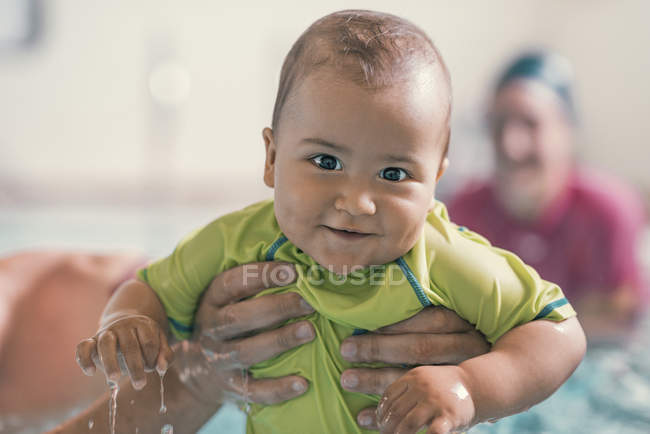 Bebê sorridente em mãos masculinas enquanto nadava aula de piscina . — Fotografia de Stock