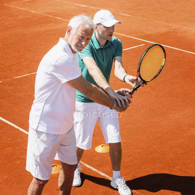 Senior pratiquant avec instructeur de tennis sur le terrain . — Photo de stock