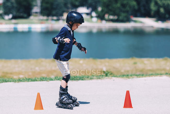 Junge übt Rollschuhlaufen im Park auf Straße mit Kegeln. — Stockfoto