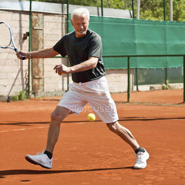 Hombre mayor activo jugando tenis en la cancha . - foto de stock