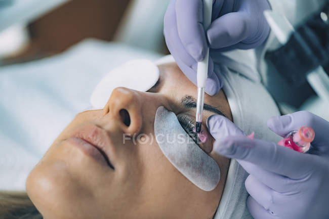 Cosmetologist putting pink paint on patient eyelashes during lash lifting and laminating procedure. — Stock Photo