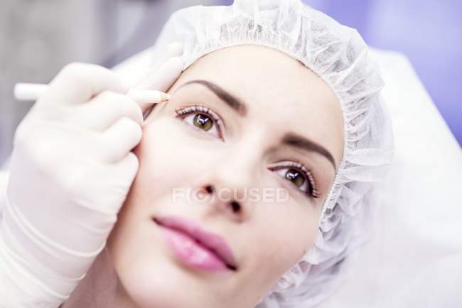 Technicien beauté utilisant un crayon pour marquer le visage féminin pour le traitement de beauté . — Photo de stock