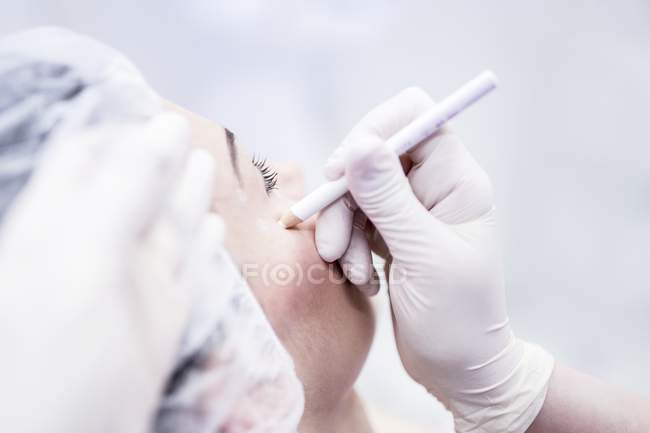 Tecnico di bellezza utilizzando la matita per contrassegnare il viso femminile per il trattamento di bellezza . — Foto stock
