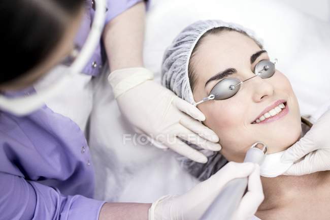 Dermatologista usando máquina de soldador a laser no rosto feminino . — Fotografia de Stock