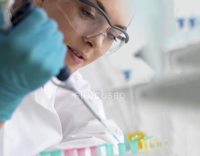 Female scientist pipetting sample into microcentrifuge tubes ready for automated analysis while biotechnology research. — Stock Photo