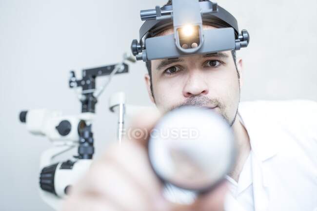 Examen indirecto del oftalmoscopio. Oftalmólogo usando un oftalmoscopio montado en la cabeza. - foto de stock