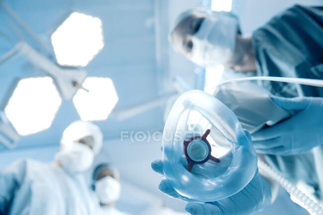 Anaesthetist placing mask on patient, surgeons in the background. — Stock Photo