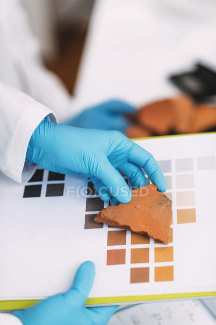 Manos del arqueólogo comparando colores de cerámica con esquema de carta de colores en laboratorio . - foto de stock