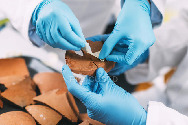 Hands of archaeologists reconstructing broken pottery in laboratory. — Stock Photo