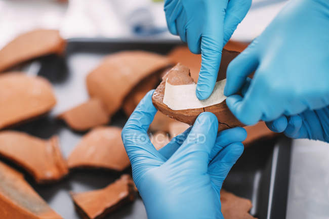 Manos de arqueólogos reconstruyendo cerámica rota en laboratorio . - foto de stock