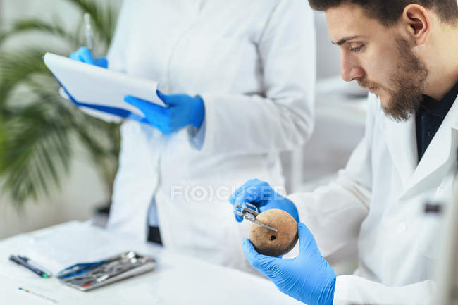 Jovem arqueólogo do sexo masculino medindo artefato antigo em laboratório . — Fotografia de Stock