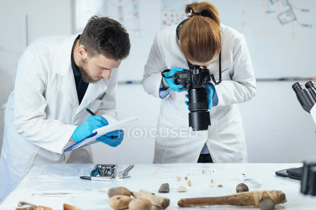 Jovens pesquisadores de arqueologia documentando litíase com câmera em laboratório e tomando notas . — Fotografia de Stock