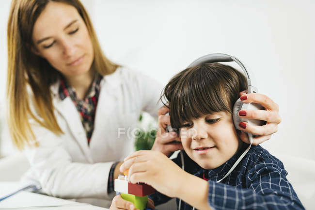 Женщина-врач надевает наушники на мальчика, который проходит тест на слух . — стоковое фото