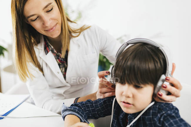 Female audiologist putting headphones on boy having hearing test. — Stock Photo