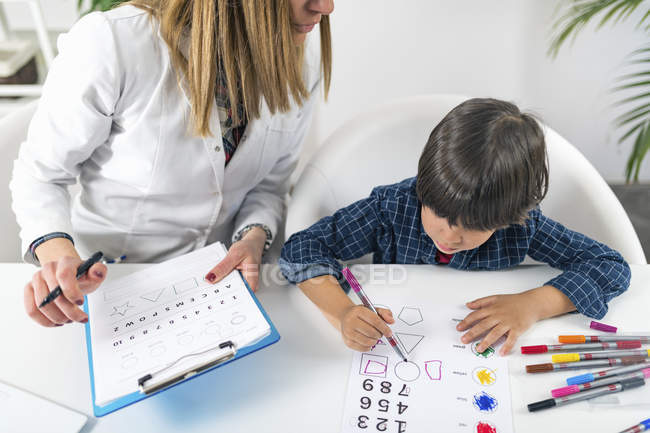 Boy coloring shapes with colorful pens for developmental psychology test in female doctor office. — Stock Photo