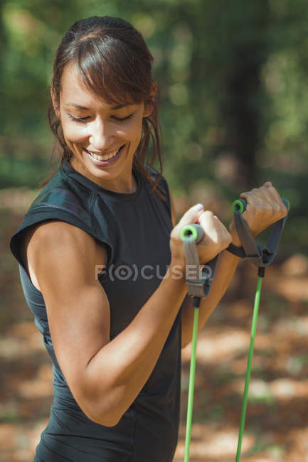 Woman smiling as exercising with elastic resistance band outdoors in park. — Stock Photo