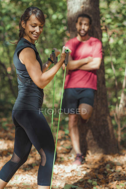Young woman exercising with elastic resistance bands with personal trainer in park. — Stock Photo