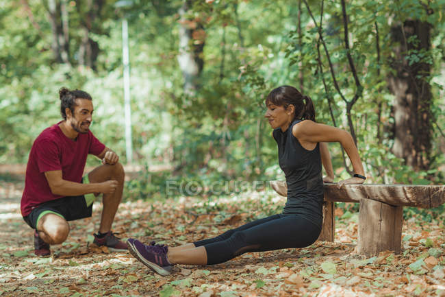 Young woman doing push-ups in park with personal trainer. — Stock Photo