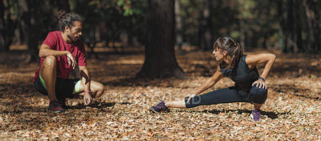 Mujer joven estirando las piernas después de entrenar con entrenador personal en el parque . - foto de stock