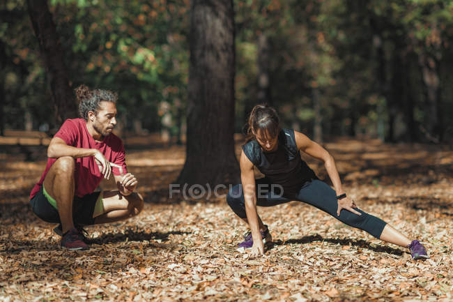 Giovane donna che allunga le gambe dopo l'allenamento con personal trainer nel parco . — Foto stock