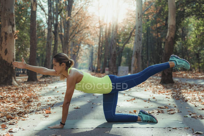 Woman doing yoga while exercising outdoors in autumn park. — Stock Photo