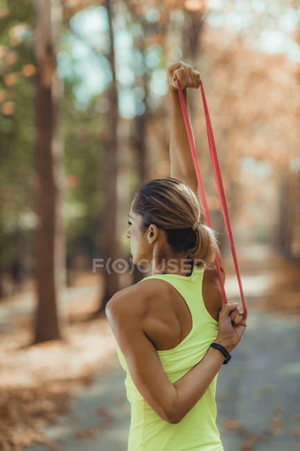Woman exercising with resistance band outdoors in autumn park. — Stock Photo