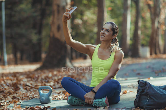 Жінка бере селфі після тренування на відкритому повітрі в осінньому парку . — стокове фото