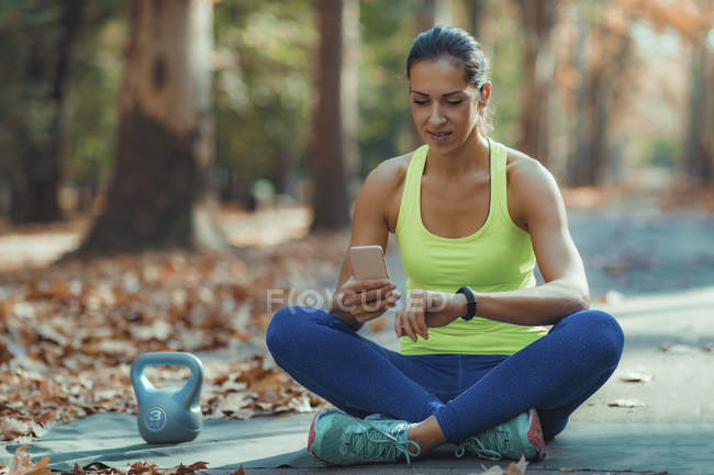 Frau überprüft Fortschritte bei Smartwatch nach Outdoor-Training im Herbstpark. — Stockfoto