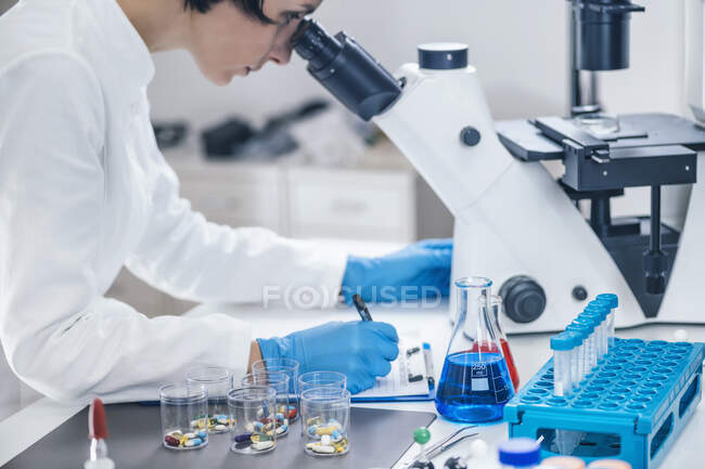 Ricercatore medico che esamina una nuova medicina. studente di scienza vestito in camice bianco guardando attraverso un microscopio. — Foto stock