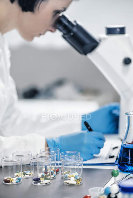 Investigador médico a examinar um novo medicamento. estudante de ciências vestida com jaleco branco olhando através de um microscópio. — Fotografia de Stock
