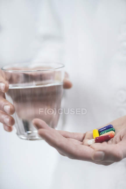 Doctor hand holding colorful pills and glass of water. — Stock Photo