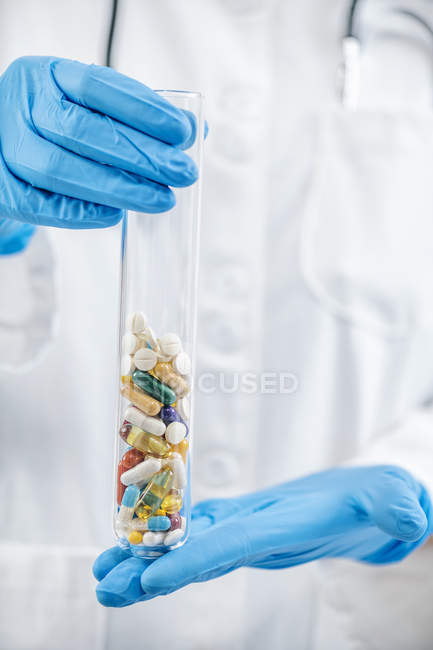 Mani scienziato farmaceutico tenendo vetro di laboratorio pieno di pillole colorate . — Foto stock