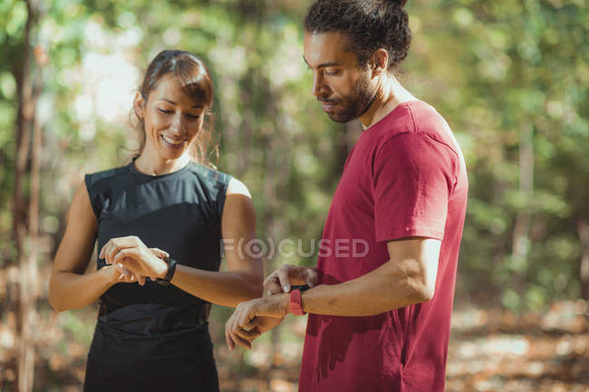 Jovens casais verificando o progresso em smartwatches enquanto treinam ao ar livre . — Fotografia de Stock