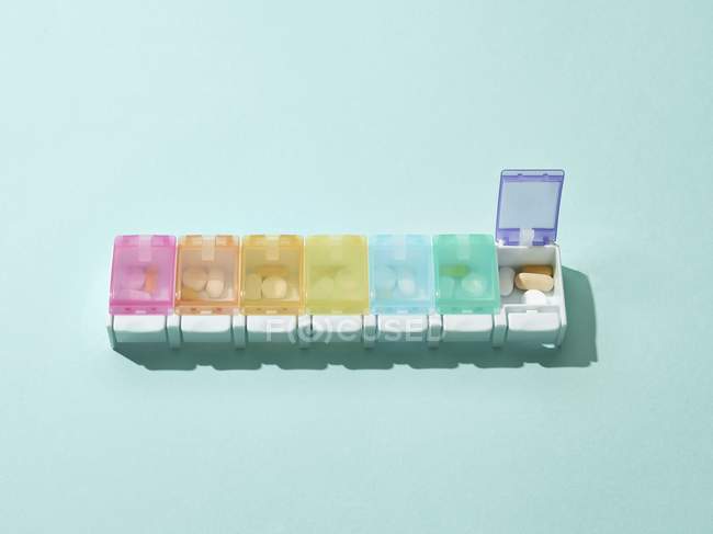 Caja de pastillas de color con siete ranuras, una ranura abierta sobre fondo azul . - foto de stock
