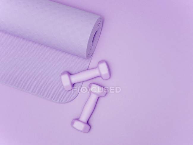 Циновка для йоги и гантели на фиолетовом фоне . — стоковое фото