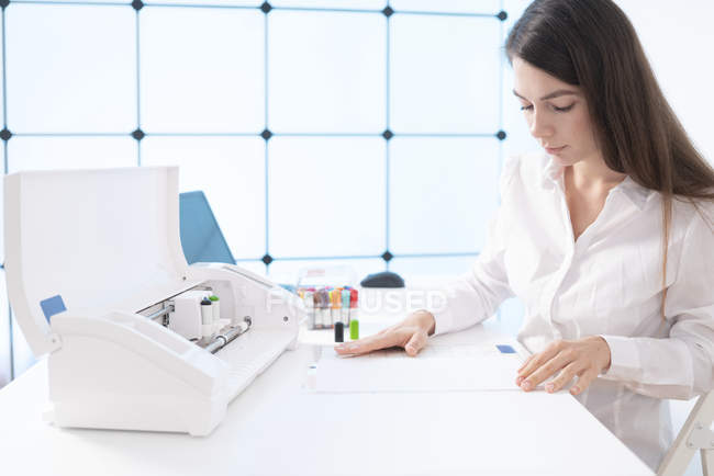 Young woman inserting paper and pens into plotter in laboratory. — Stock Photo