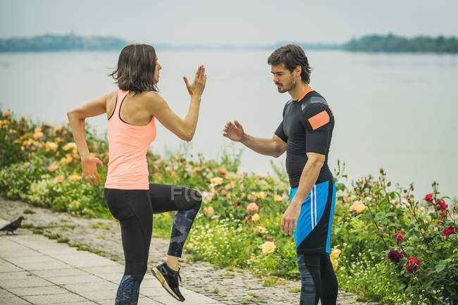 Young woman exercising and lifting legs by river with personal trainer. — Stock Photo