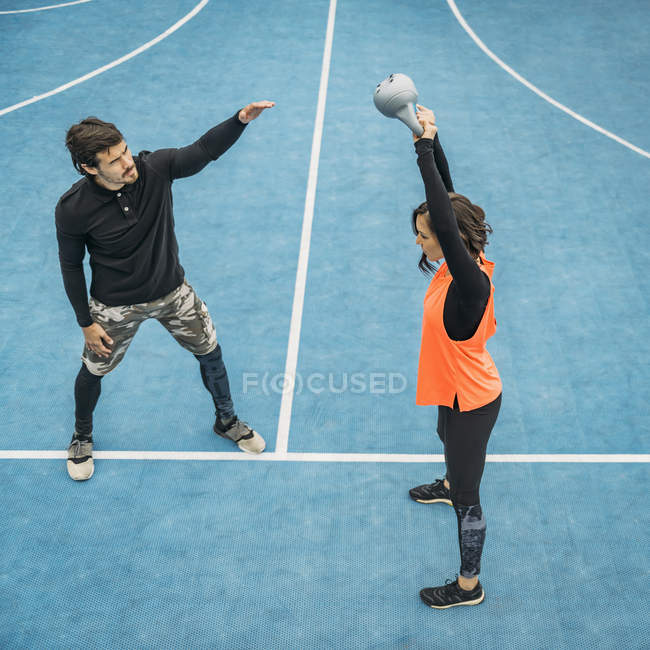 Молодая женщина размахивает гирей на открытом воздухе с помощью тренера по фитнесу . — стоковое фото
