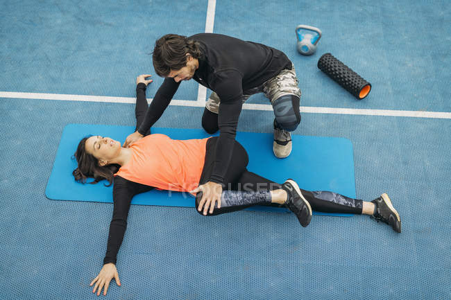 Adatta giovane donna che fa esercizio di stretching dopo l'allenamento con personal fitness trainer . — Foto stock
