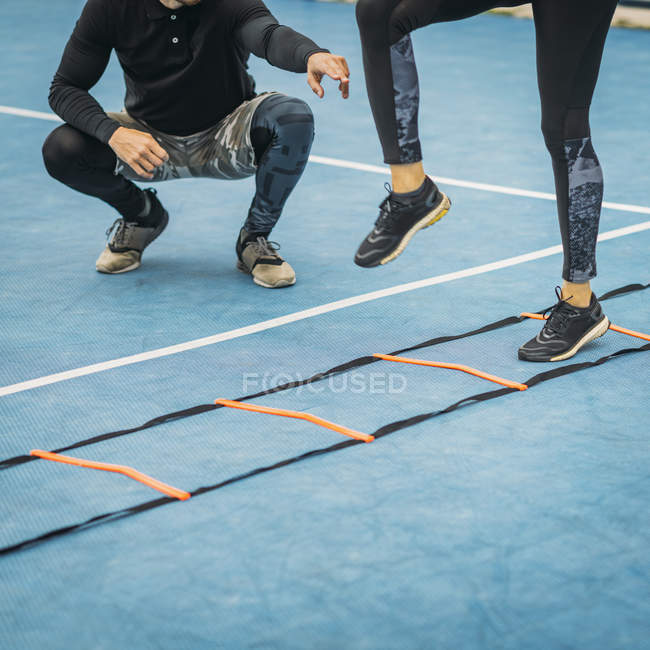 Gambe di donna che si esercita con personal fitness coach utilizzando la scala di agilità . — Foto stock