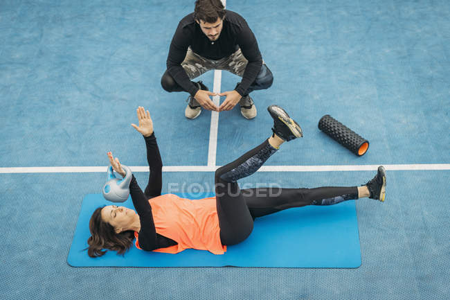 Особистий фітнес-тренер, що працює з молодою жінкою, робить вправи з чайником на відкритому повітрі . — стокове фото