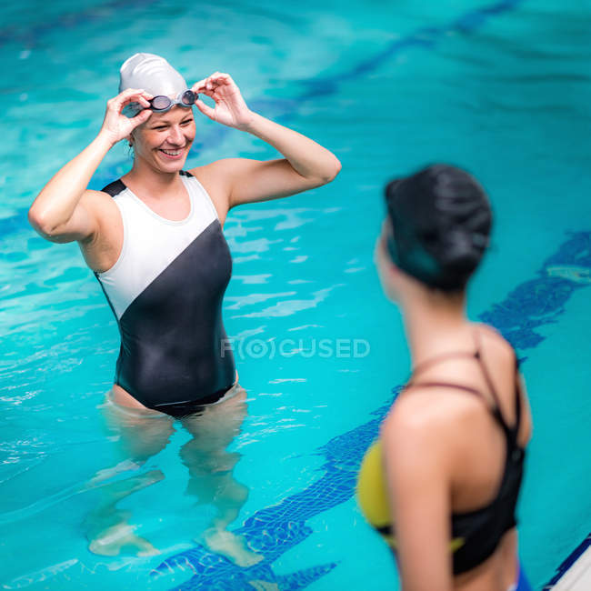 Alegres nadadoras hablando mientras descansan junto a la piscina en la piscina cubierta . - foto de stock