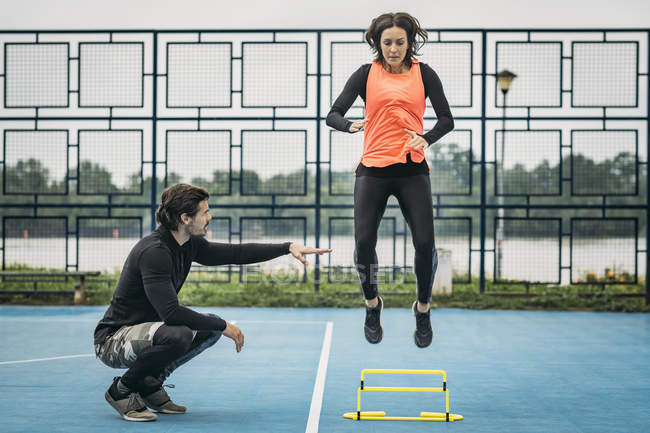 Donna sportiva che salta oltre l'ostacolo con assistenza allenatore di fitness . — Foto stock