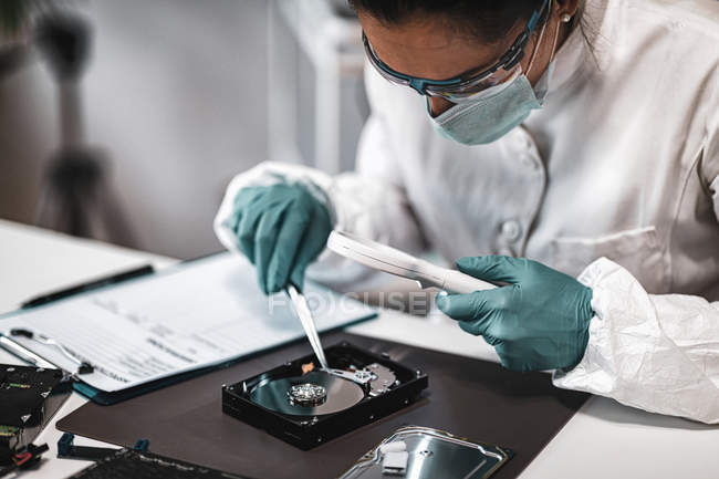 Digital forensic science technician examining computer hard drive with magnifying glass in laboratory. — Stock Photo
