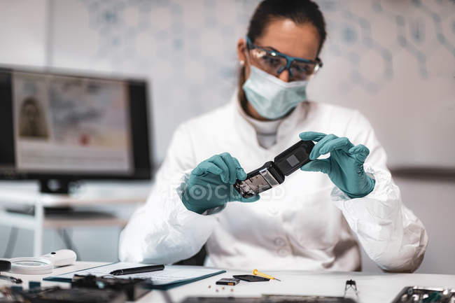 Analista forense digital feminina examinando telefone celular confiscado . — Fotografia de Stock