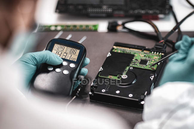 Female digital forensic expert examining computer hard drive with electronic equipment in police science laboratory. — Stock Photo