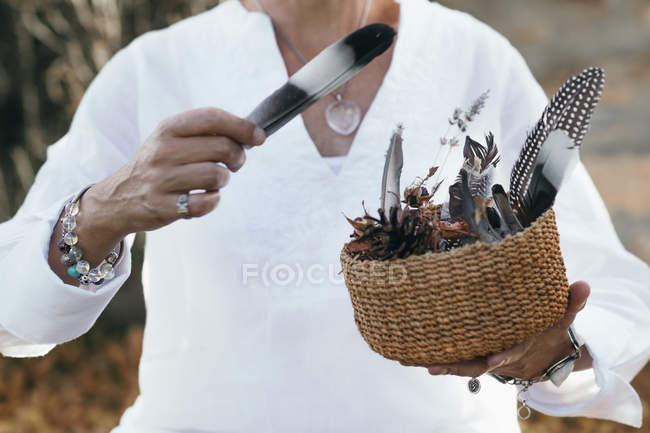 Female shaman in white clothing working with feathers, midsection. — Stock Photo